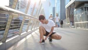 Ethnic focused young sportsman lacing shoes before training on street in city