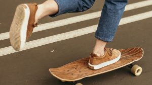 Person in Blue Denim Jeans and Brown Shoes Standing On A Skateboard on Gray Concrete Road