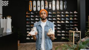 Bearded Man in Denim Vest Holding a Pair of White Shoes