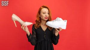Portrait of Expressive Woman Holding Sneakers and Heeled Shoes Isolated on Red Studio Background